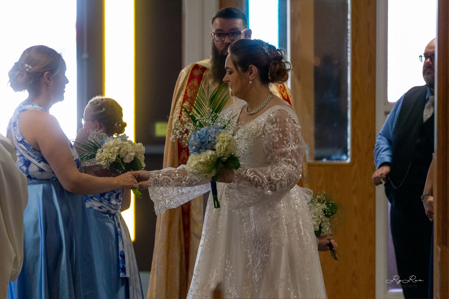 A wedding ceremony in progress with attendants in blue dresses and the bride in a lace gown.