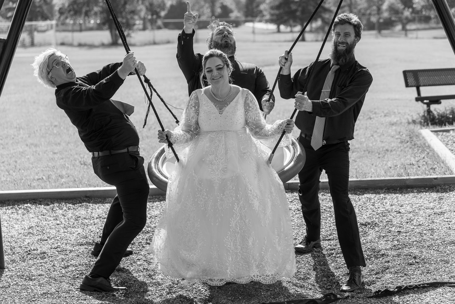 Black and white photo of people having fun on playground swings during a wedding celebration.
