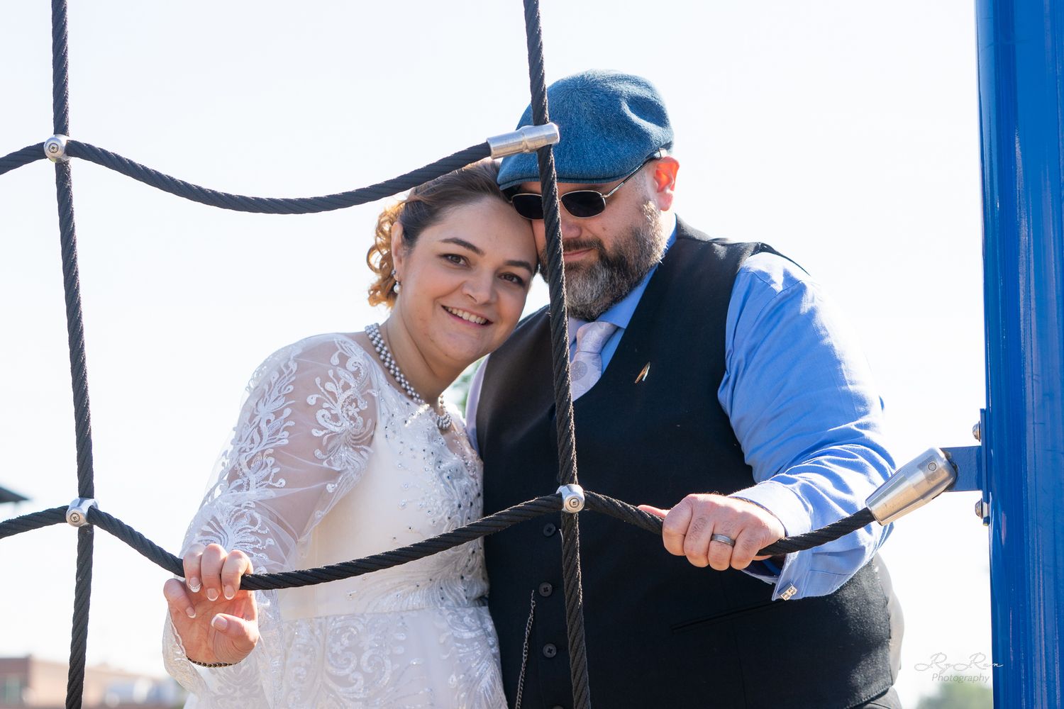 A happy couple poses together behind blue ropes during their wedding day.