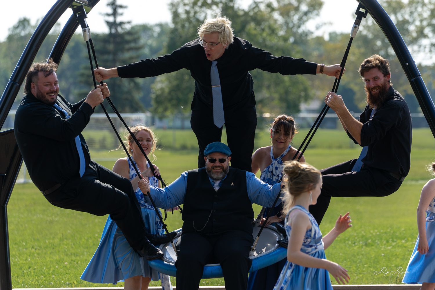 Playful wedding group poses on outdoor playground equipment with matching blue outfits.