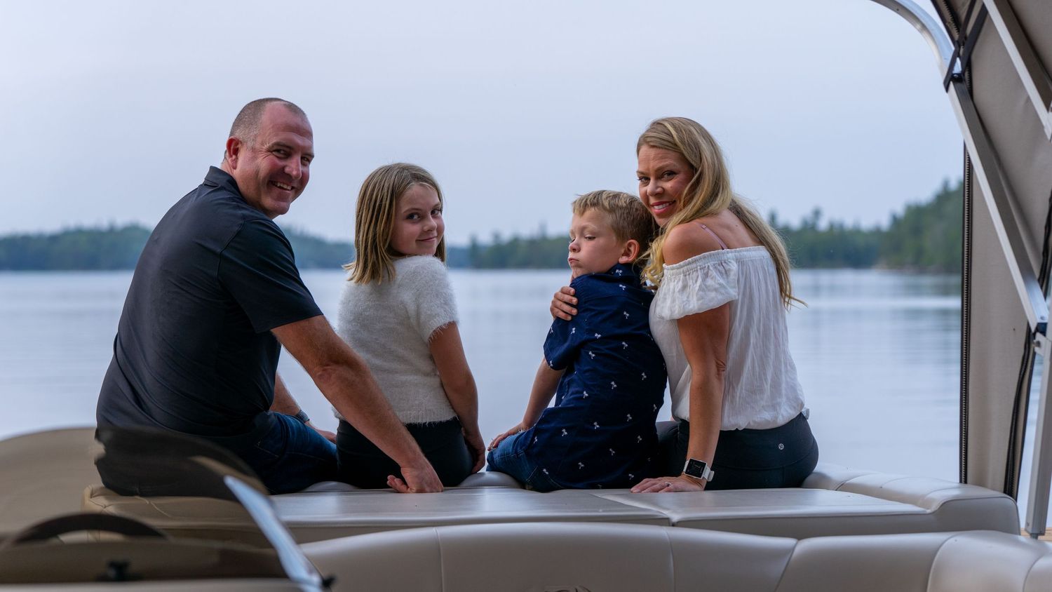 Family sitting together on boat deck with lake view in background.