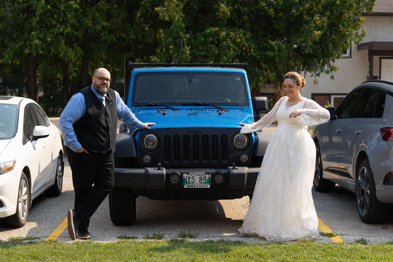 Wedding photo featuring white dress and blue Jeep in parking lot.