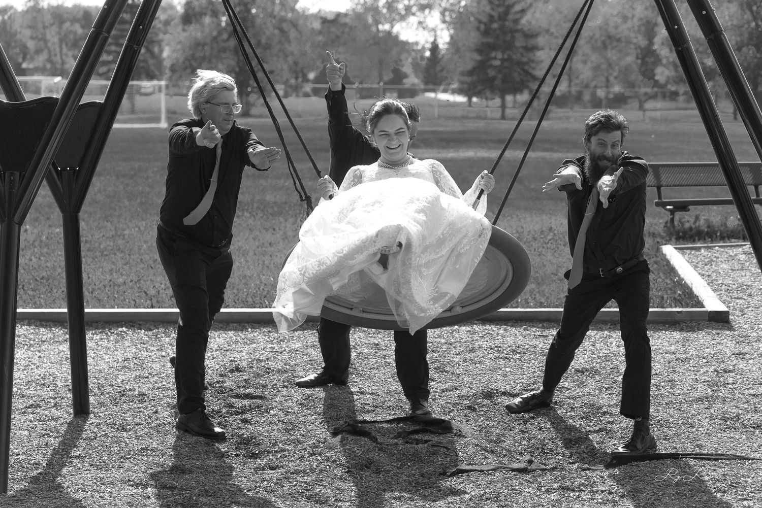 Black and white capture of playful wedding party members on swing set.