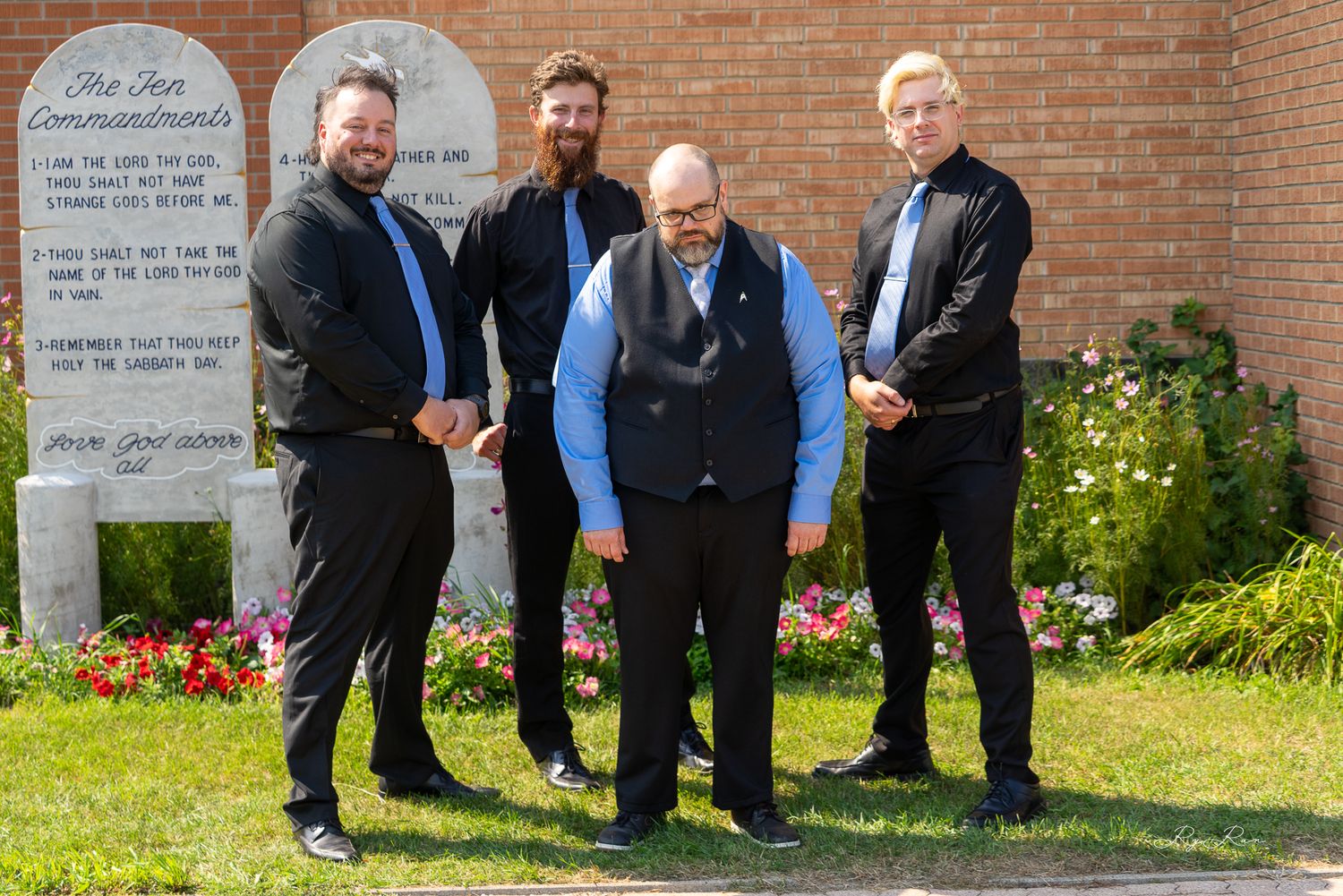 Group portrait of four people in formal attire standing by stone tablets and flowers.