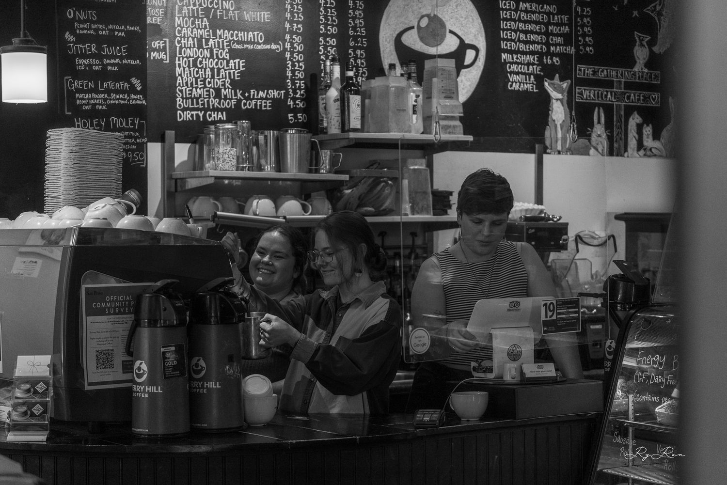 Interior view of a busy coffee shop counter with menu board and espresso equipment.