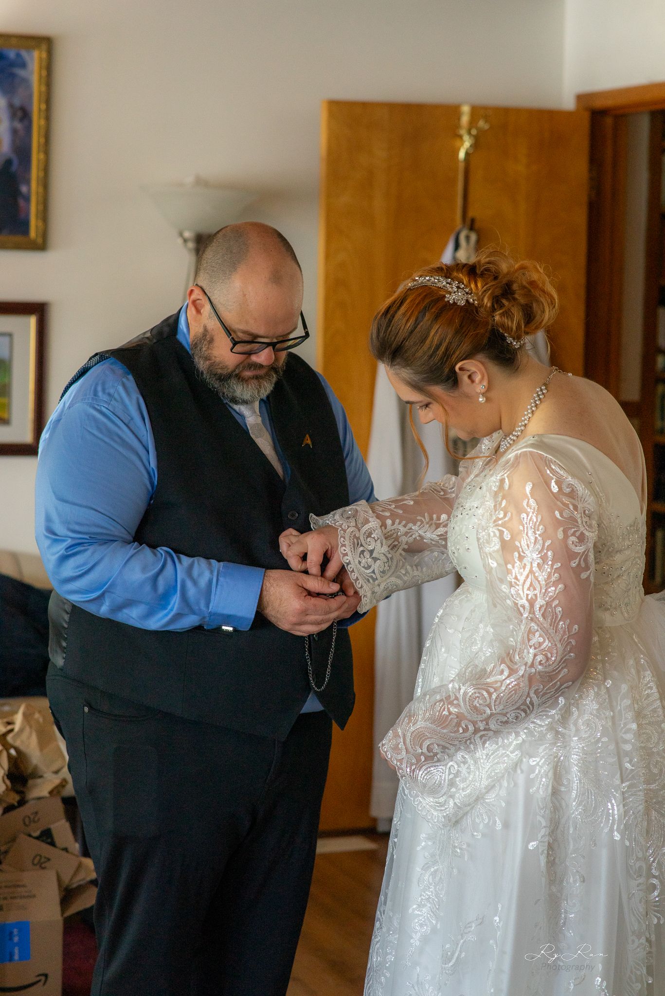 A tender moment as a bride and companion share a special pre-wedding preparation moment in a lace gown and blue shirt.