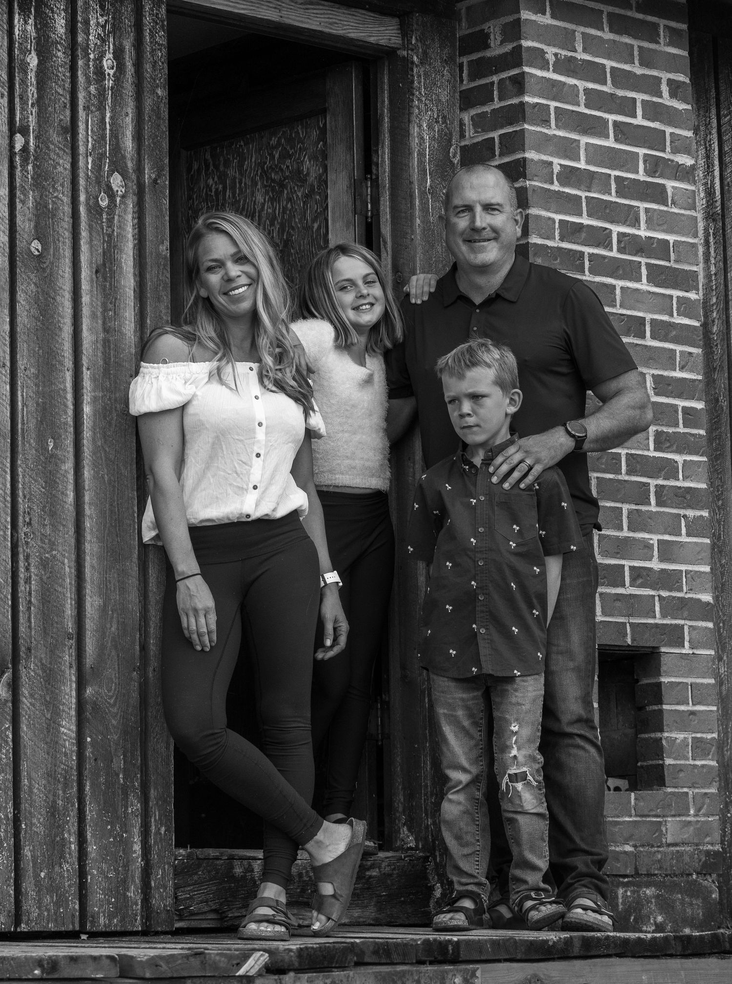 Black and white portrait of family standing in rustic doorway entrance.