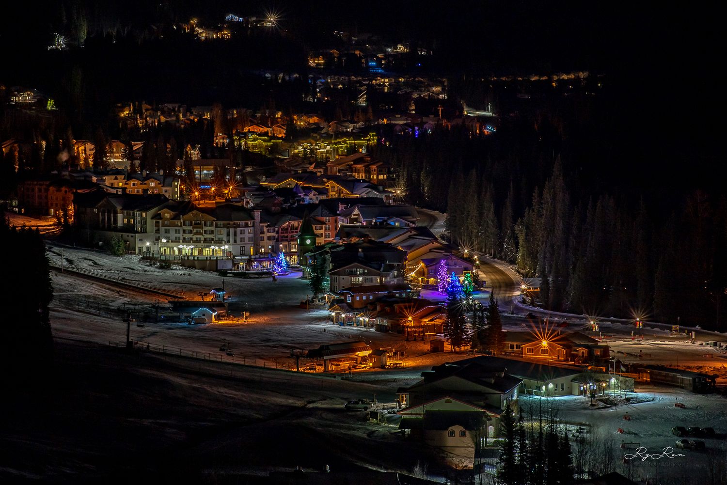 Ski resort illuminated at night with colorful lights glowing against dark mountain backdrop.