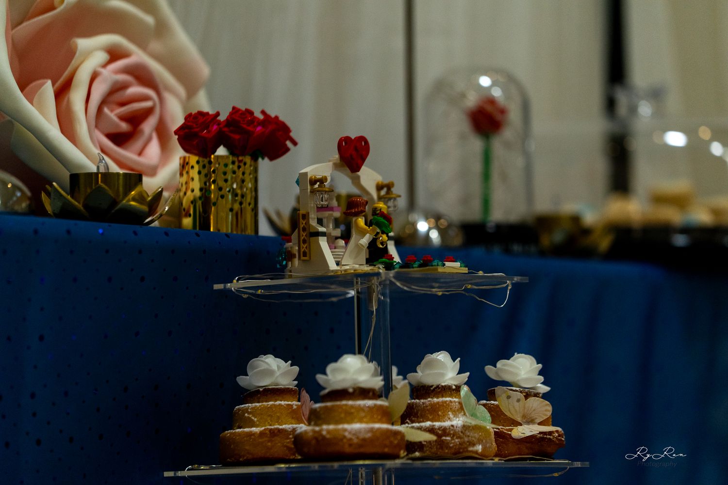 Multi-tiered dessert stand with mini cakes displayed against a blue backdrop with pink roses.