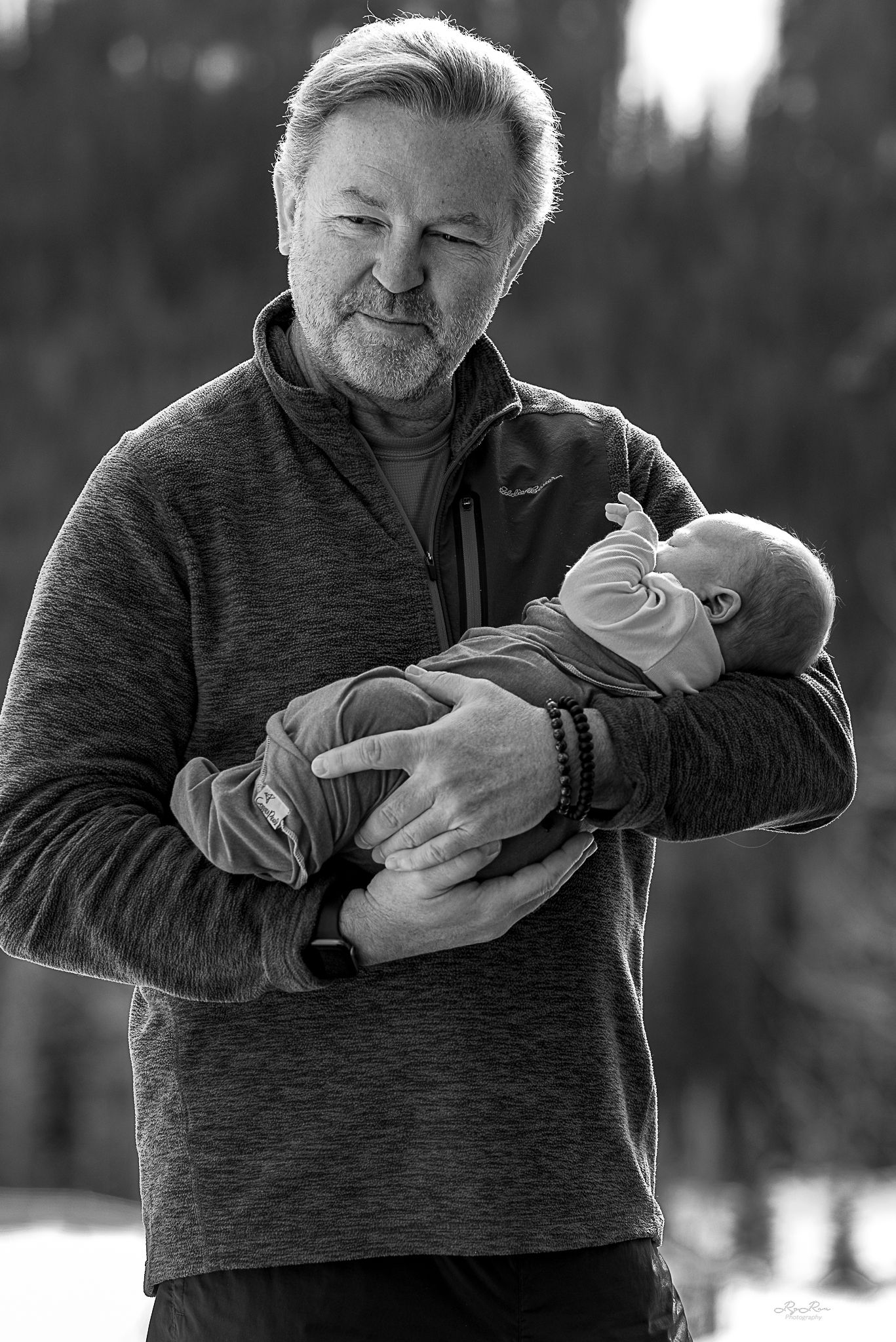 Black and white portrait of person in fleece holding sleeping infant outdoors in winter setting.