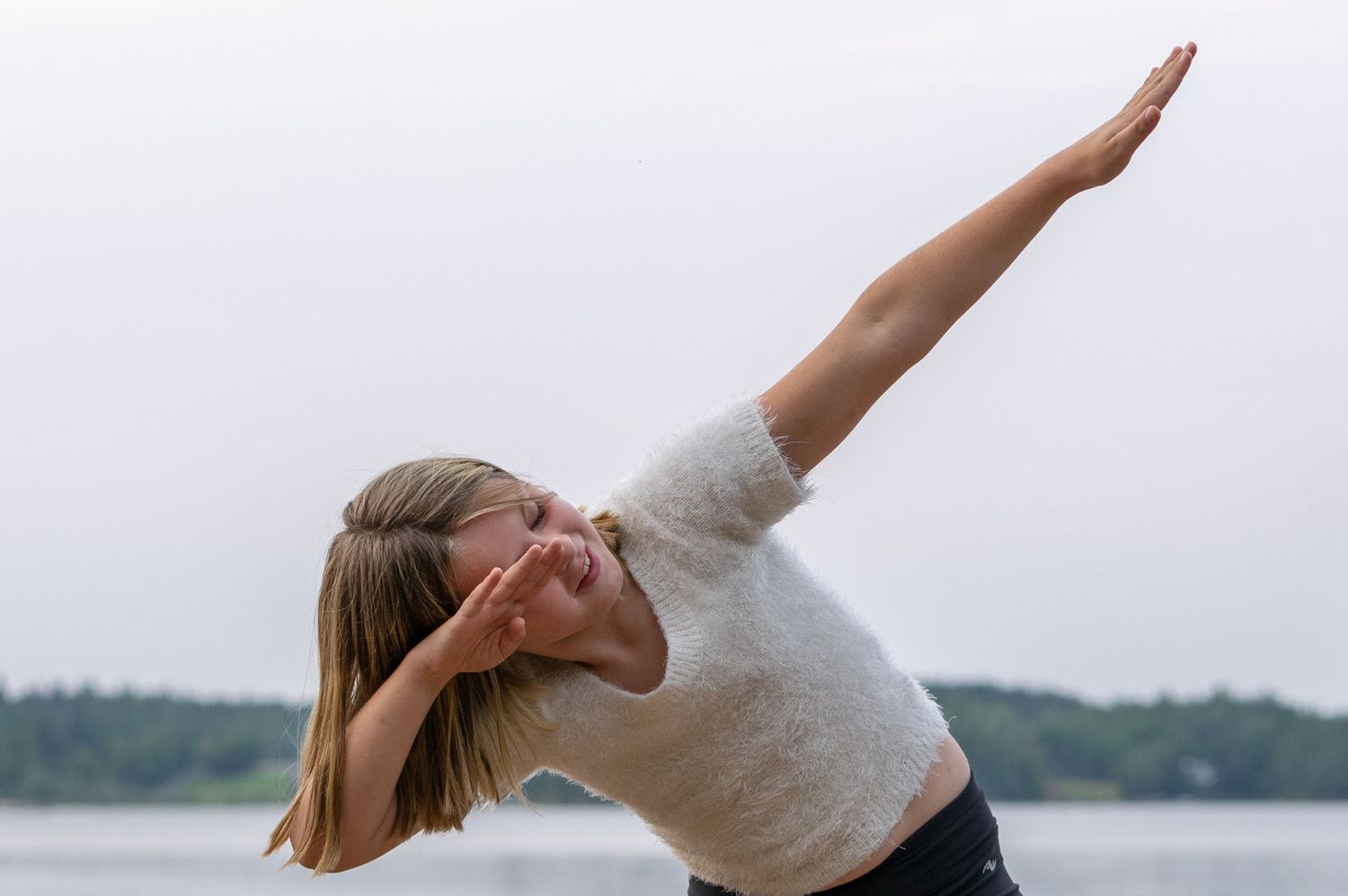 A graceful yoga pose performed on a dock by the water at dusk.