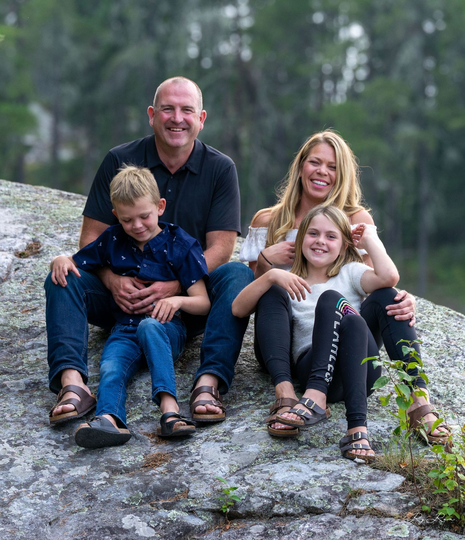 A small group sits together on a granite rock formation surrounded by greenery.