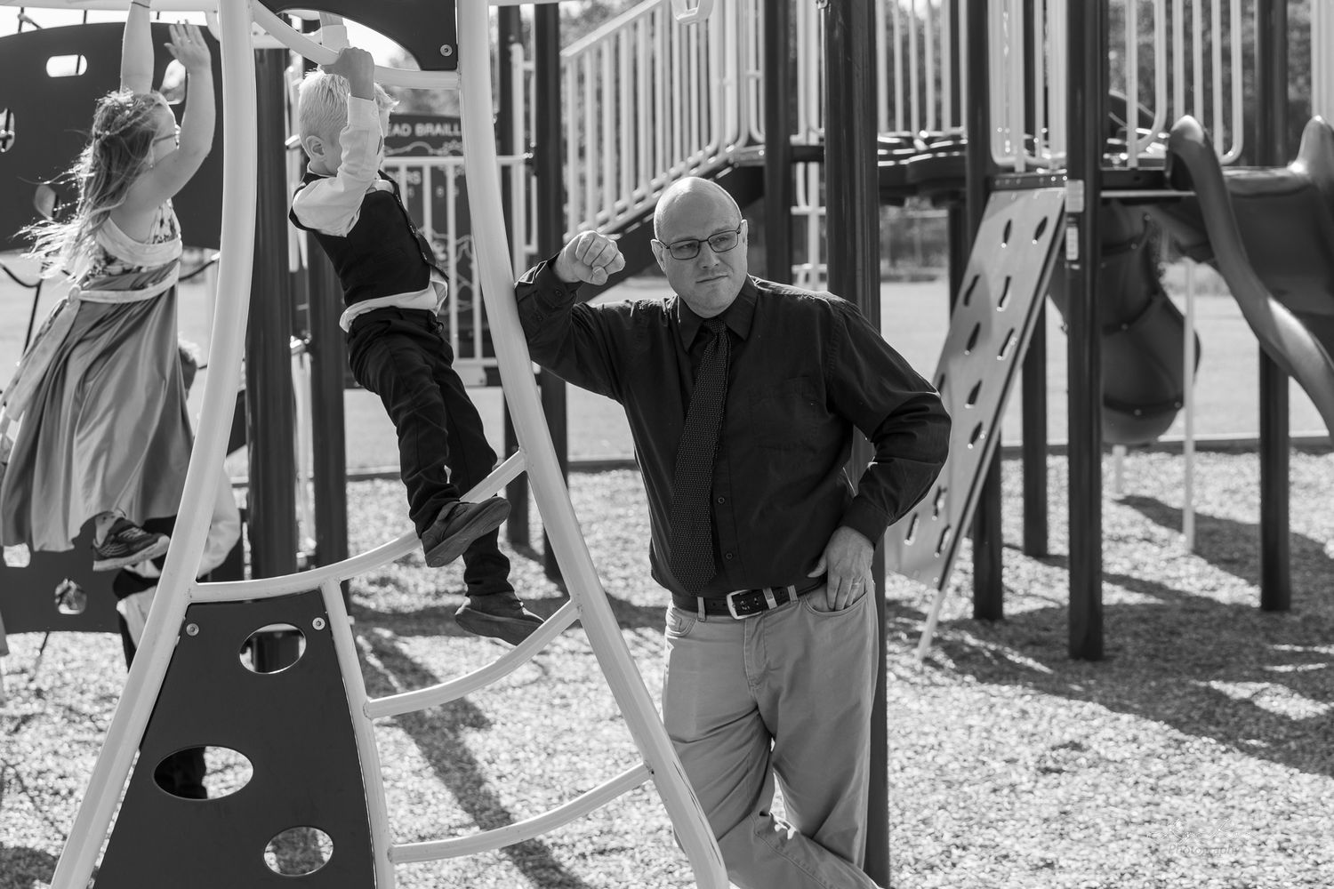 Black and white photo of people in formal wear posing on playground equipment.