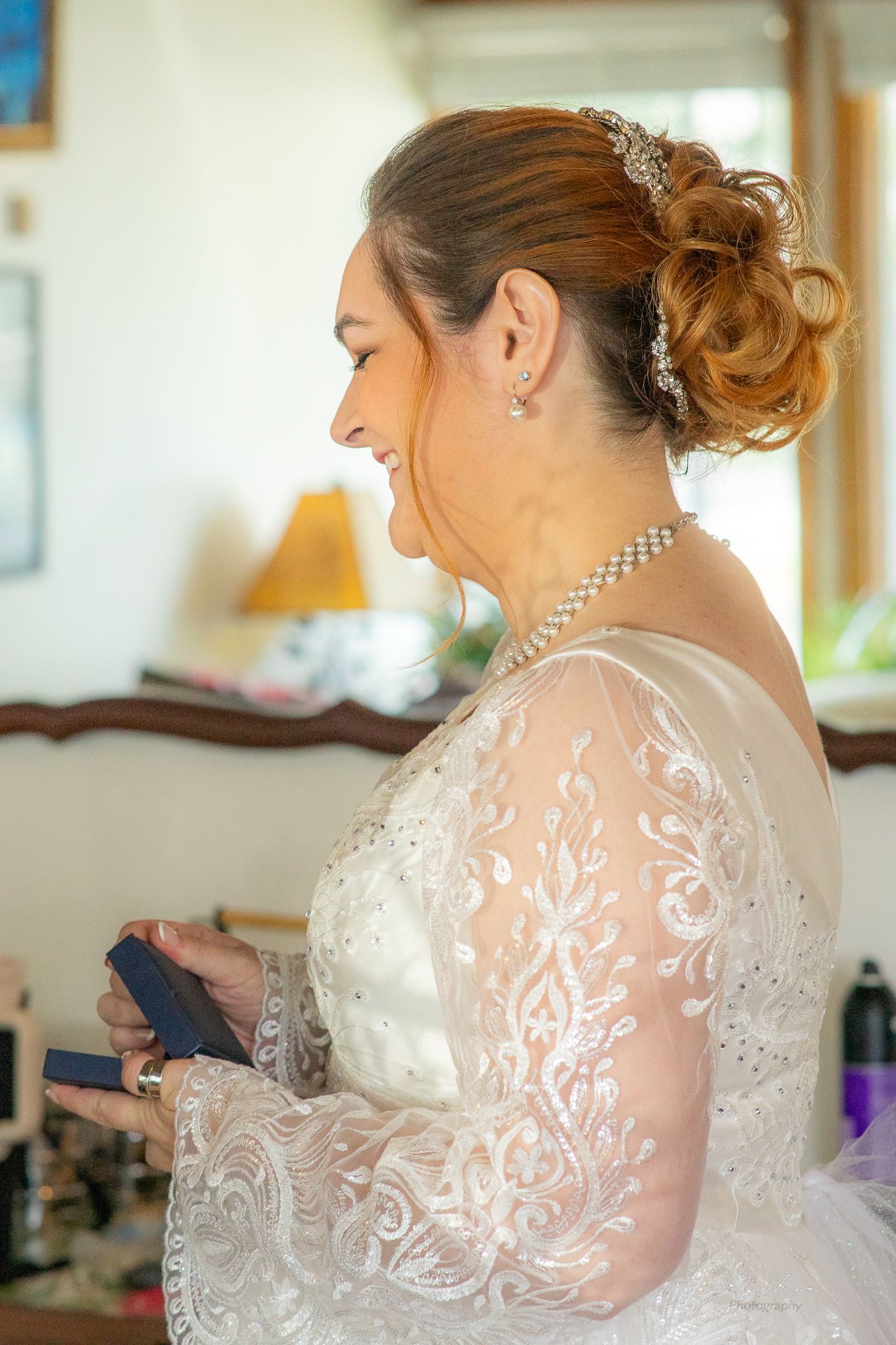 Side profile of a bride with updo hairstyle wearing lace wedding dress and pearl necklace.