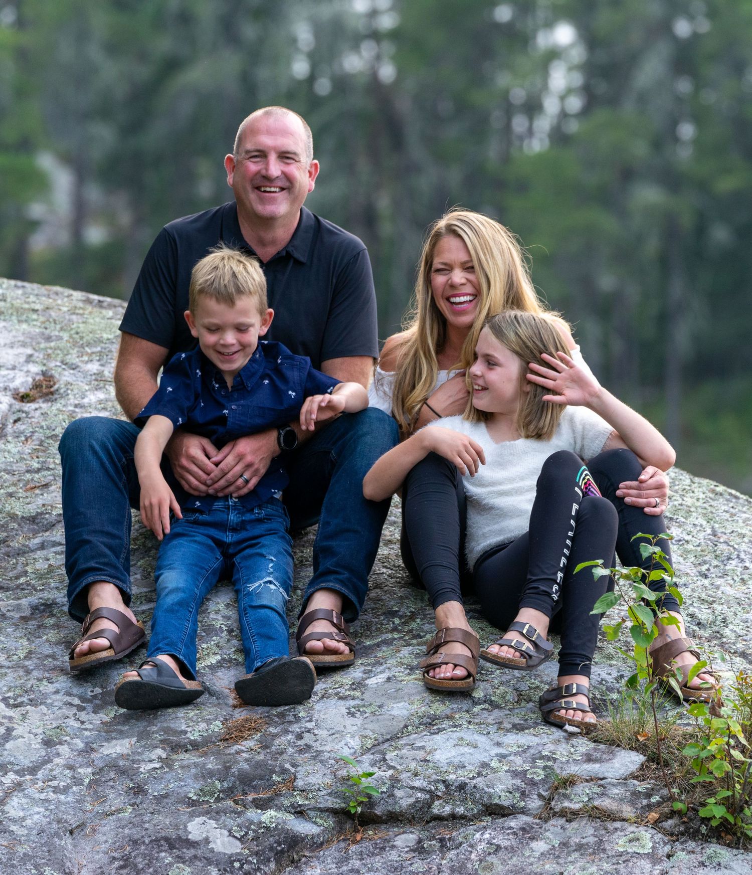 A happy family sits together on a rocky outcrop surrounded by forest scenery.