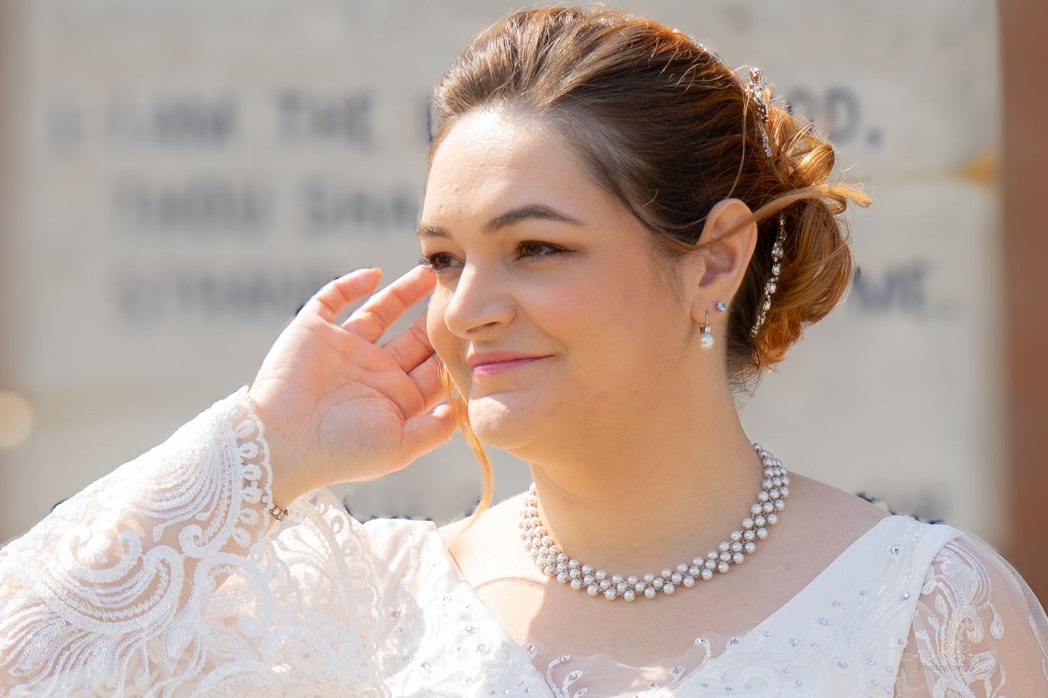 A close-up portrait of a bride wearing an elegant lace gown and pearl necklace on her wedding day.