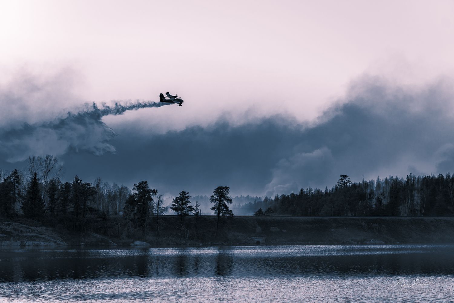 Silhouette of aircraft flying over misty lake landscape at dusk.