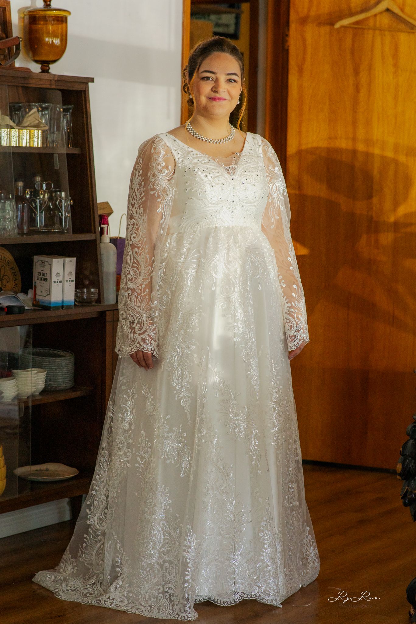 A full-length portrait of a bride in a flowing white lace wedding gown with sheer sleeves.