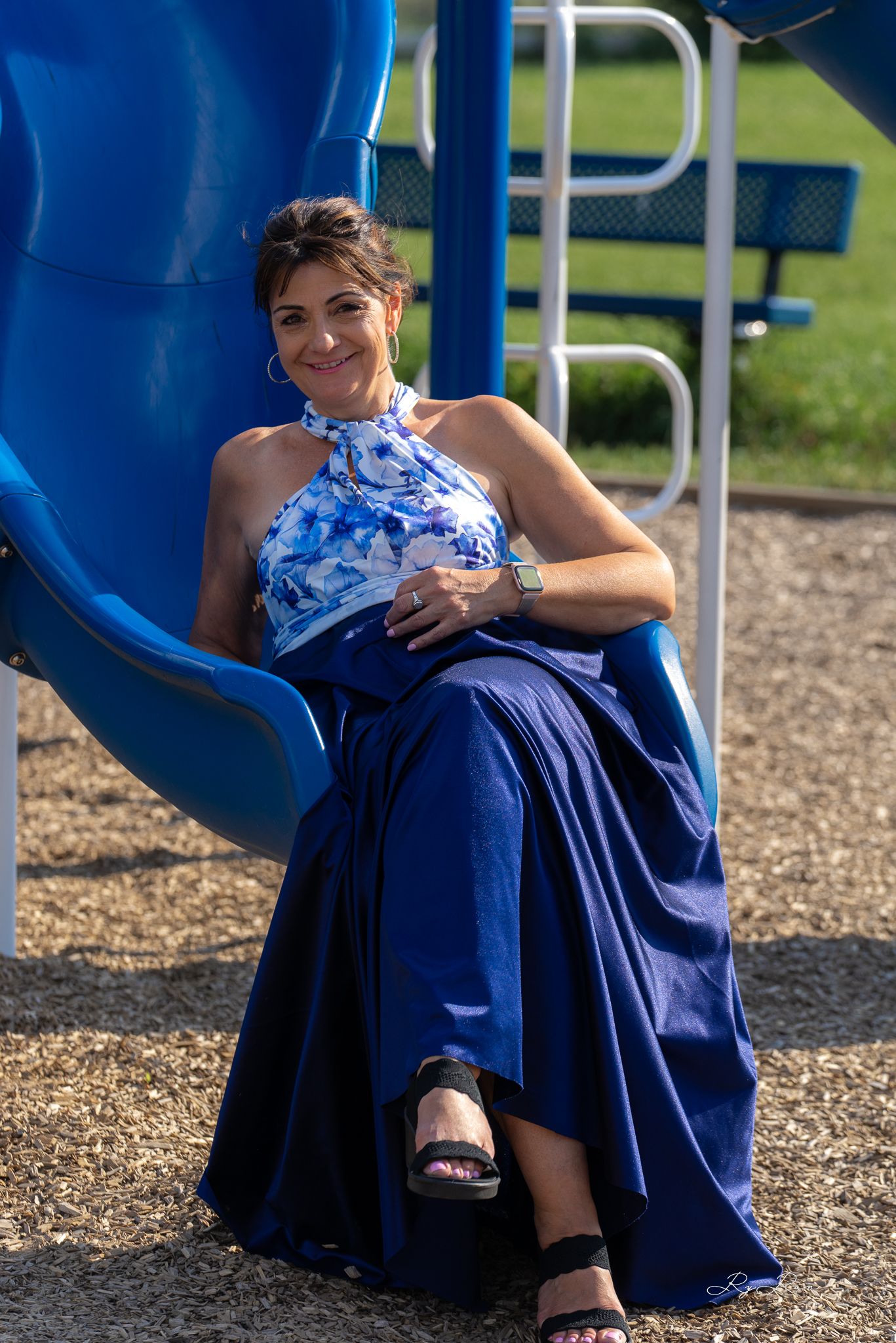 Woman in blue formal dress sitting elegantly on playground equipment.