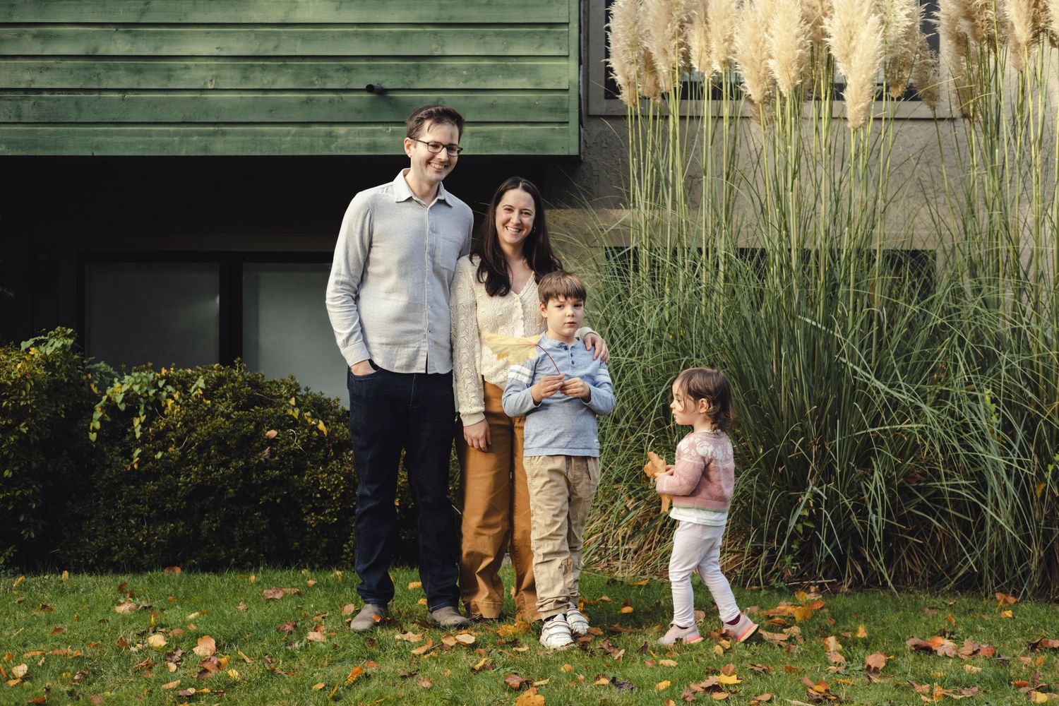 Family portrait session in a garden with rustic green walls and ornamental grasses in the background.