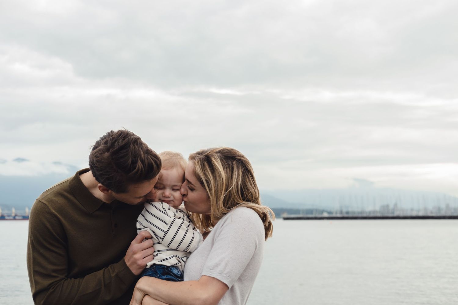 Family sharing tender moment together by waterfront on cloudy day.