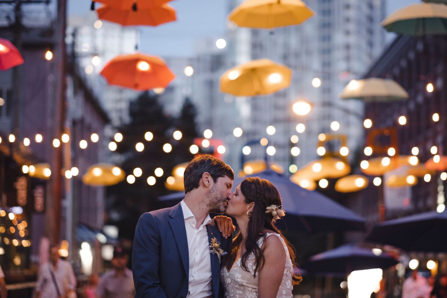 Romantic couple sharing intimate moment under colorful suspended umbrellas and string lights.