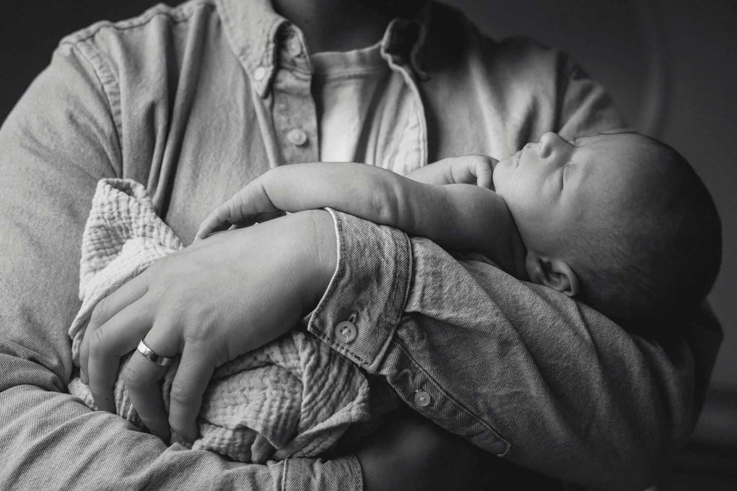 Sleeping newborn baby rests peacefully against caregiver wearing denim.