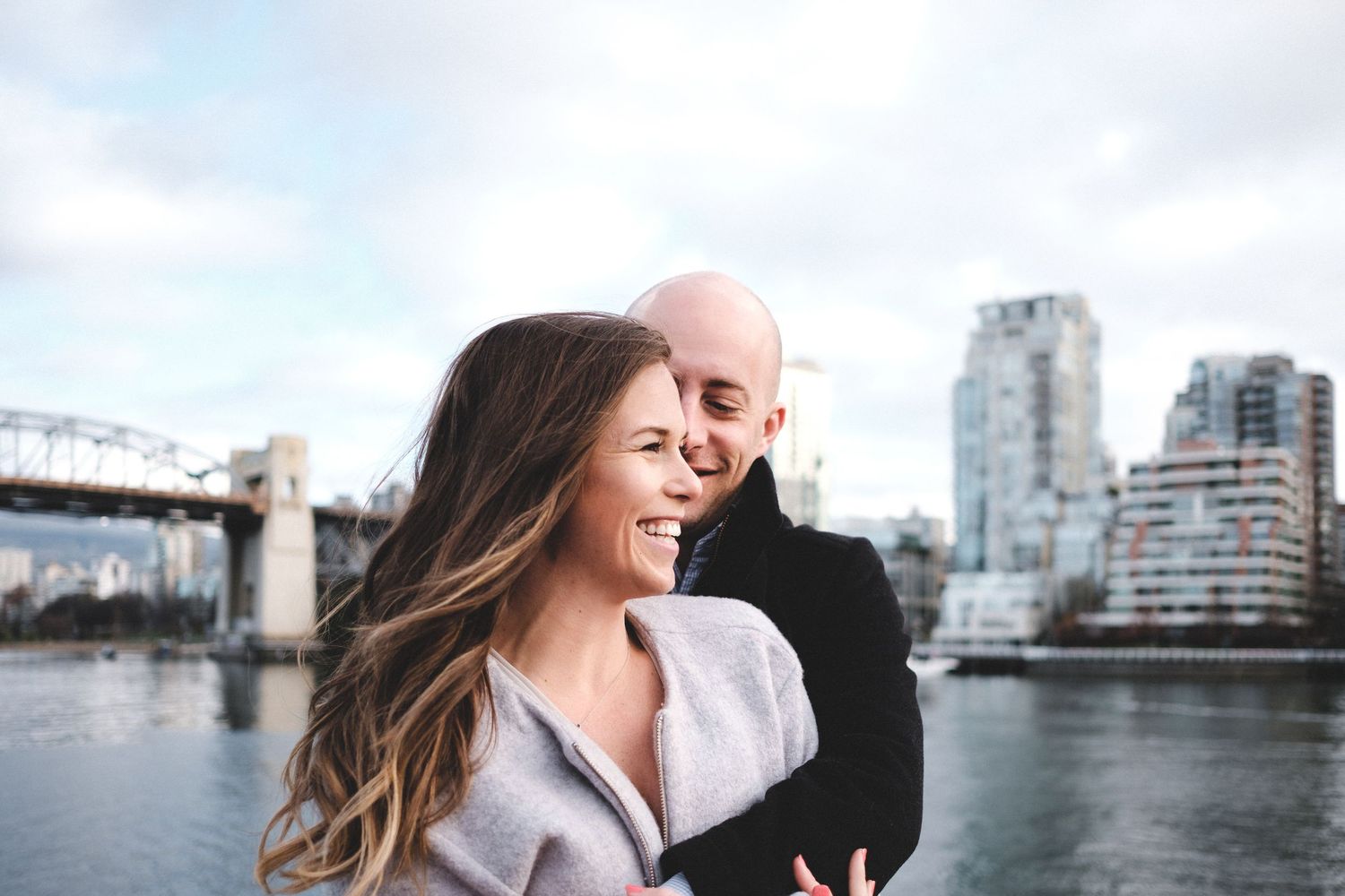 Couple laughing together with city bridge and skyline in background.