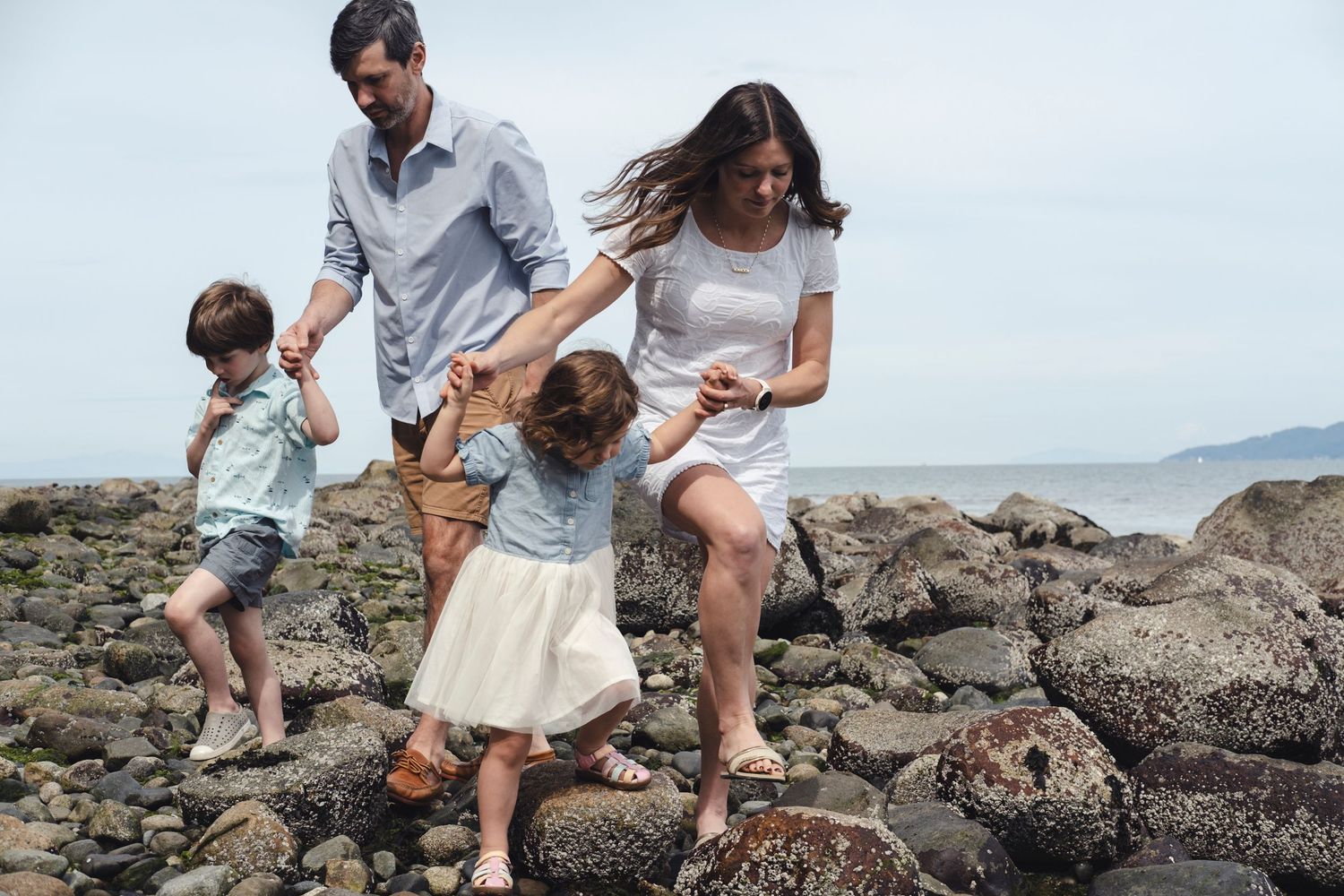 Family exploring rocky beach tidepools together on sunny coastal afternoon.