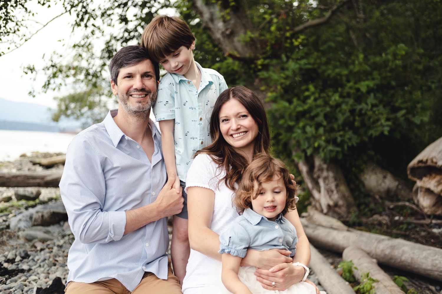 Family of three enjoying a relaxed outdoor portrait session among lush green trees and natural scenery.