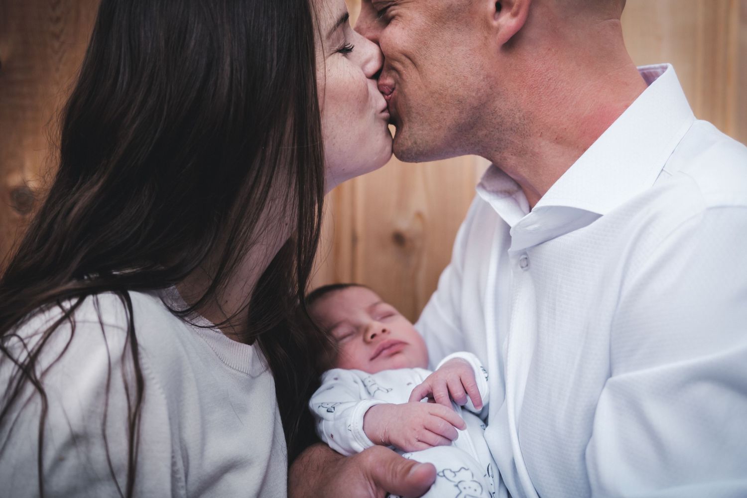 Intimate family moment as parents kiss while holding their newborn baby.