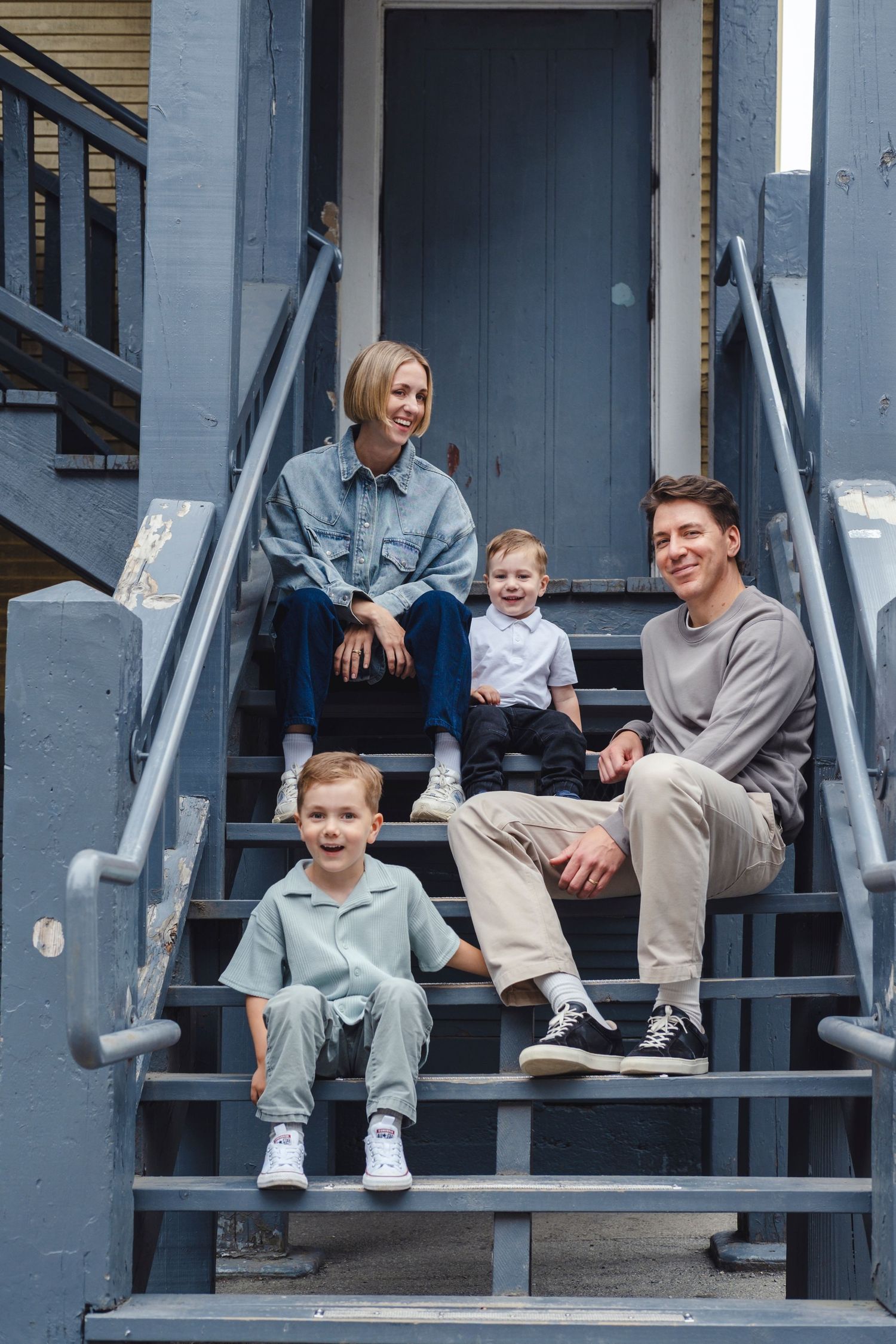 Family sits together on gray wooden porch steps sharing casual moments and laughter.