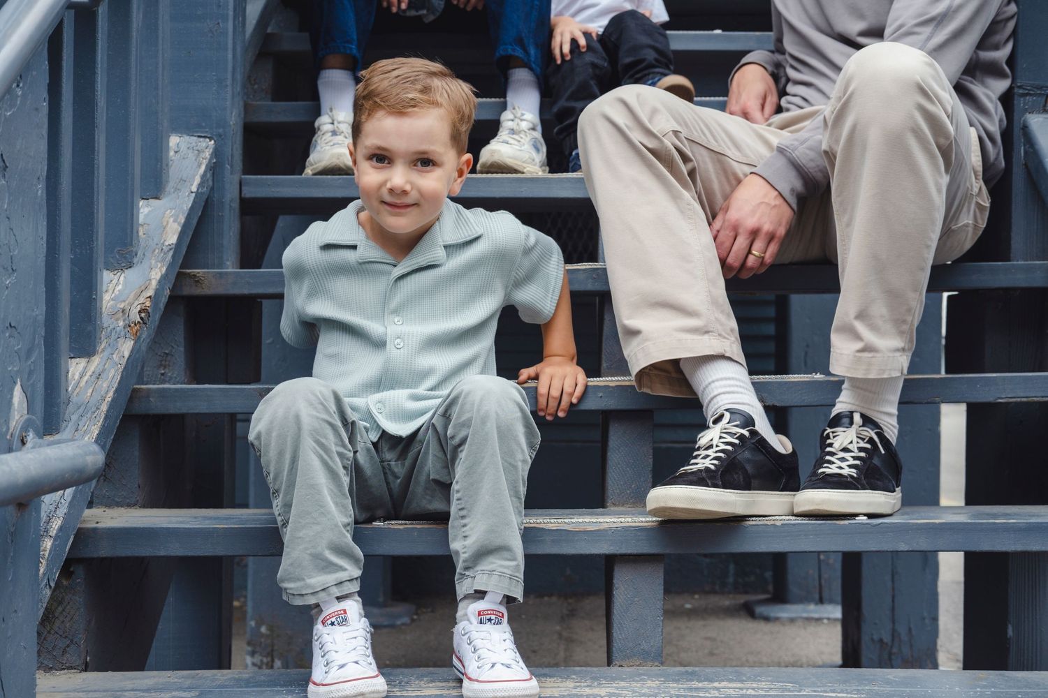 Baseball fans sit in stadium bleachers wearing casual clothing and sneakers on a sunny day.