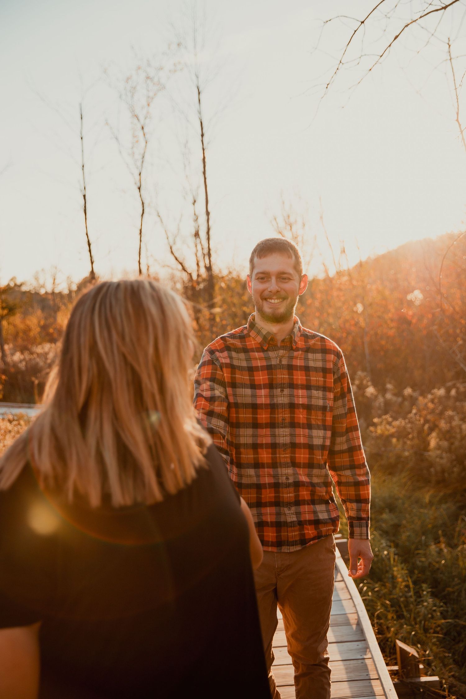 A couple shares a moment on a wooden boardwalk during golden hour in autumn. couples engagement