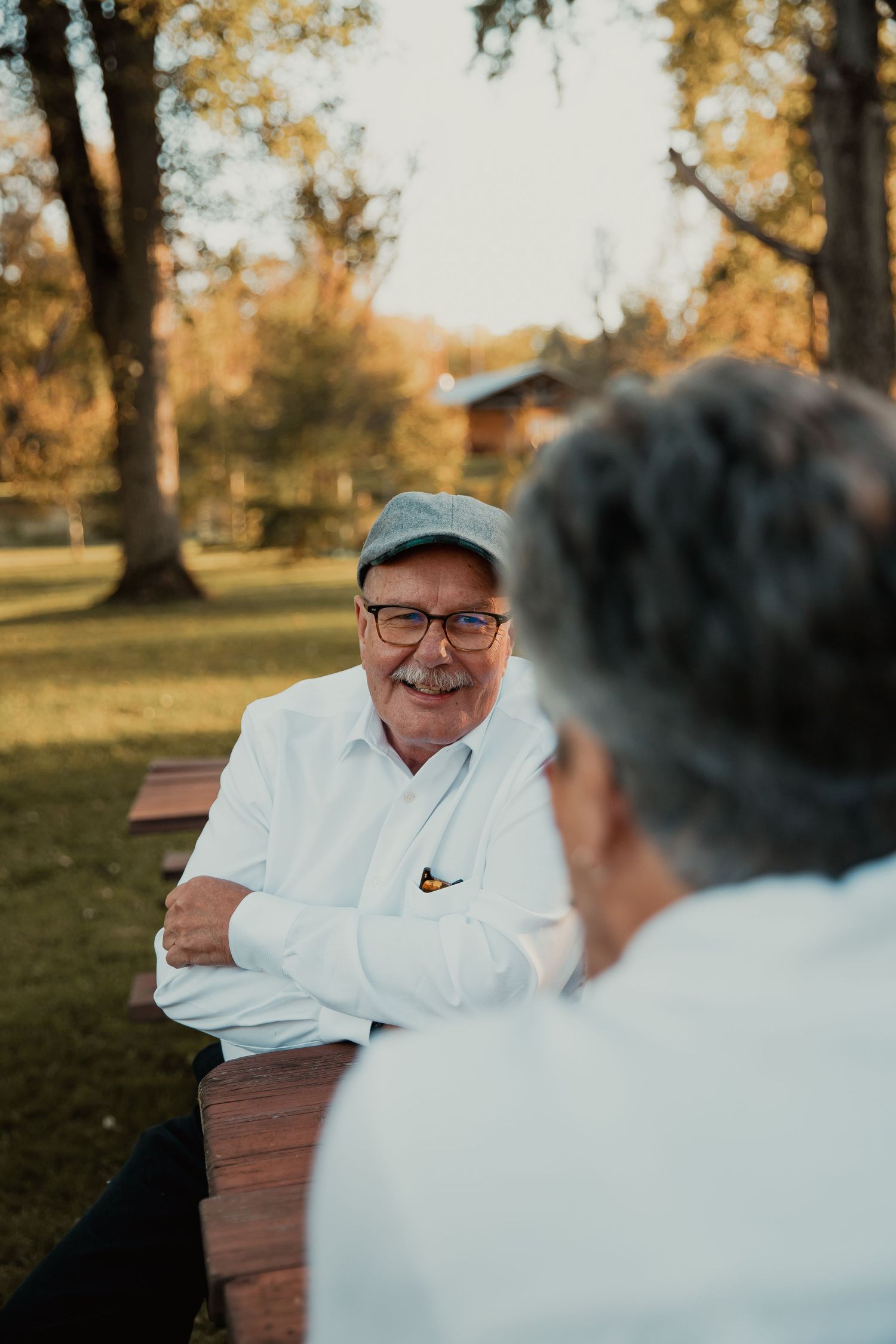 Person in cap and white shirt smiling at picnic table during golden hour. couples engagement