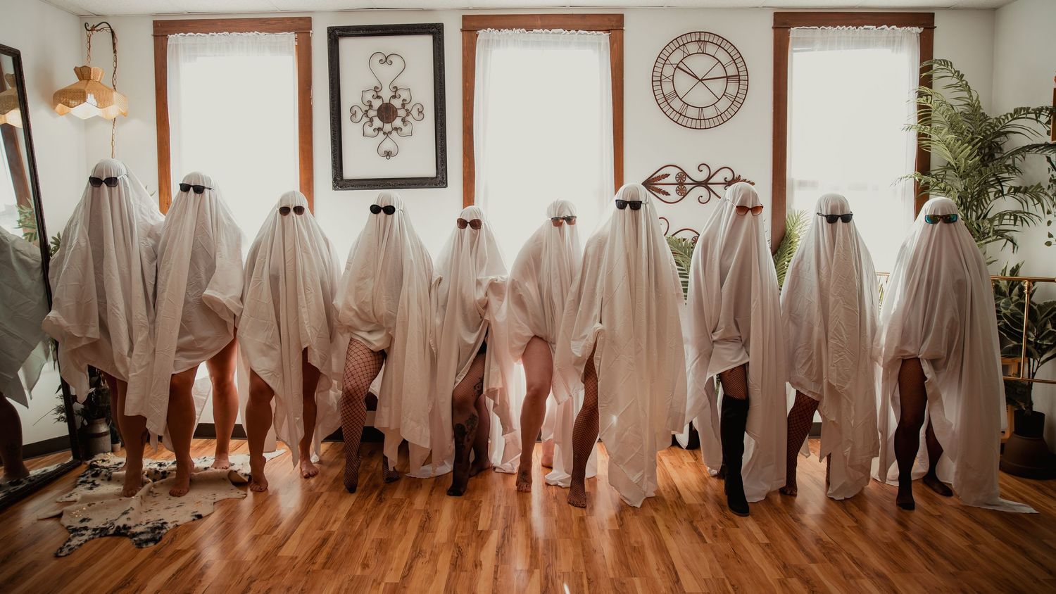 A row of people wearing white sheets standing in a rustic room with windows and wall art decor.