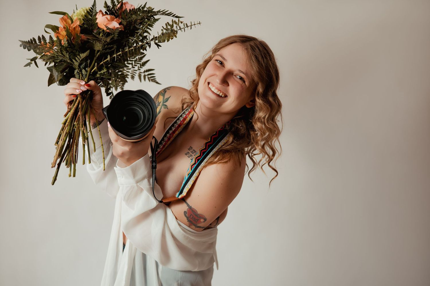A person in a white dress holds a vibrant autumn-colored floral bouquet against a neutral backdrop.