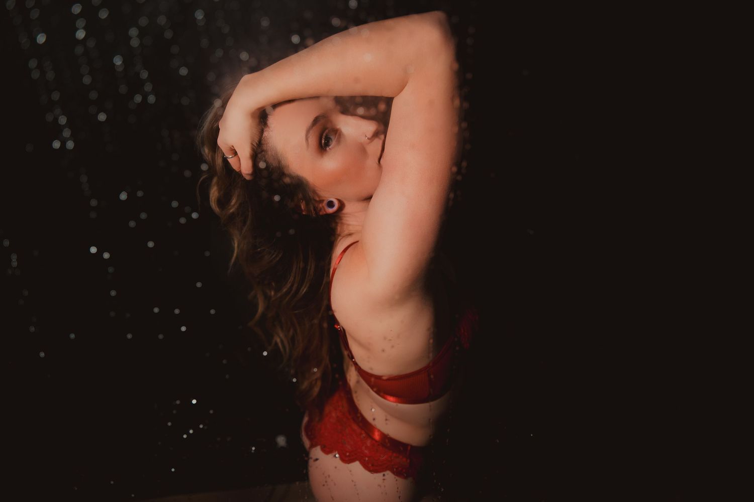 Artistic boudoir photo with burgundy lingerie against dark background with glittering water droplets.