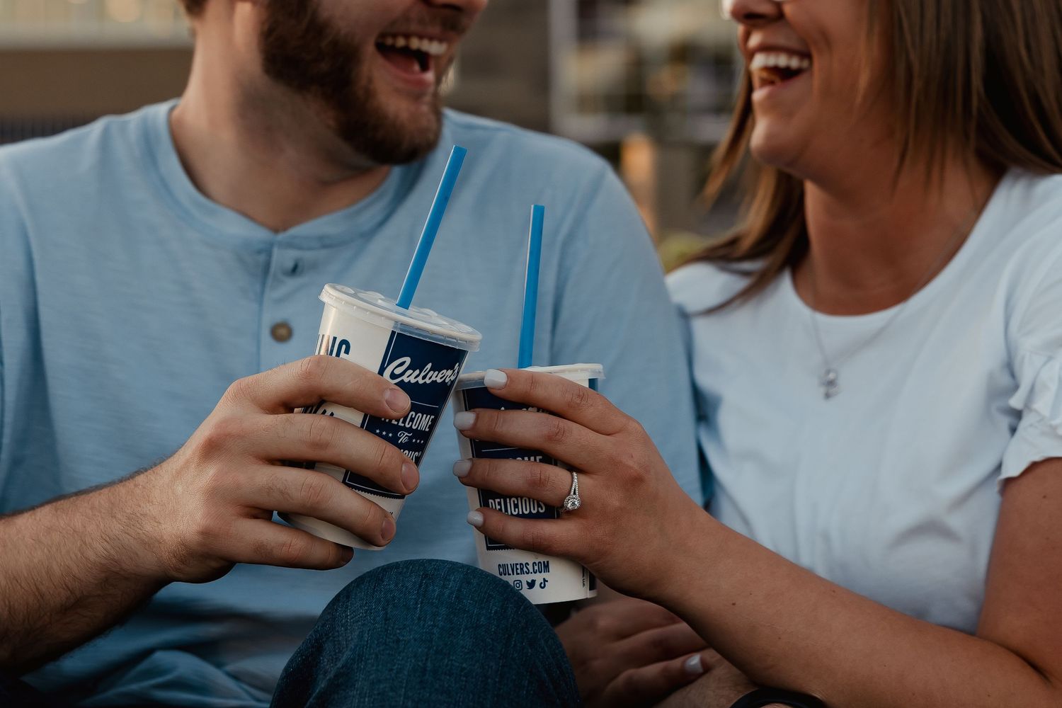 Couple laughing and toasting with Culver's frozen custard drinks on a sunny day.