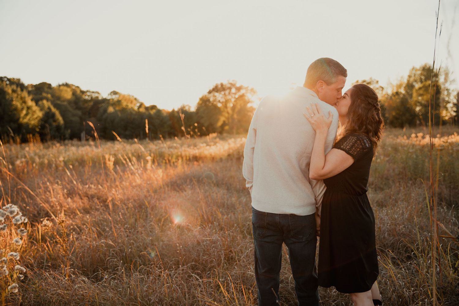 A couple embraces in a golden field during sunset with warm backlighting. couples engagement