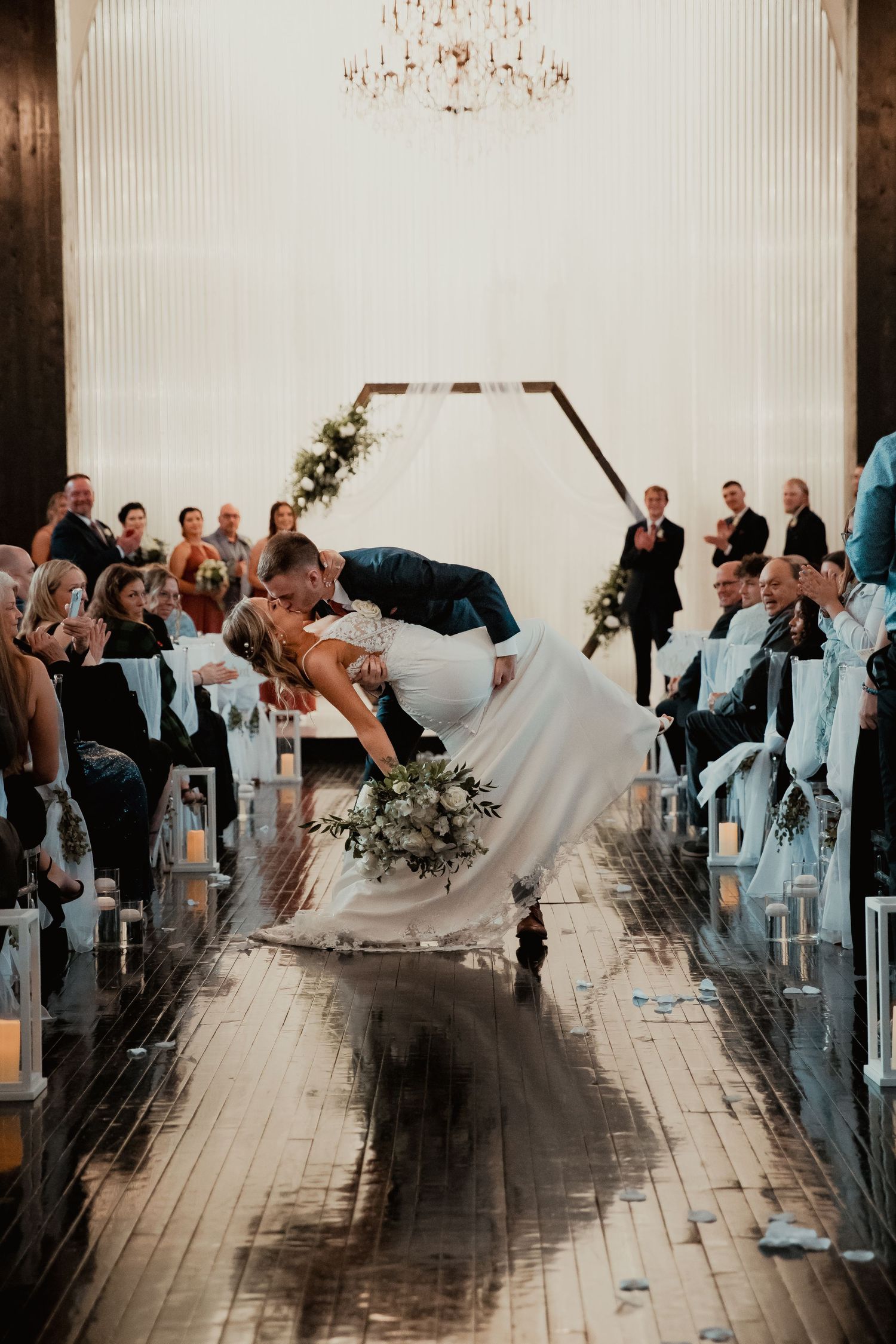A dramatic dip during a wedding ceremony captured under an elegant chandelier on a reflective floor. wedding