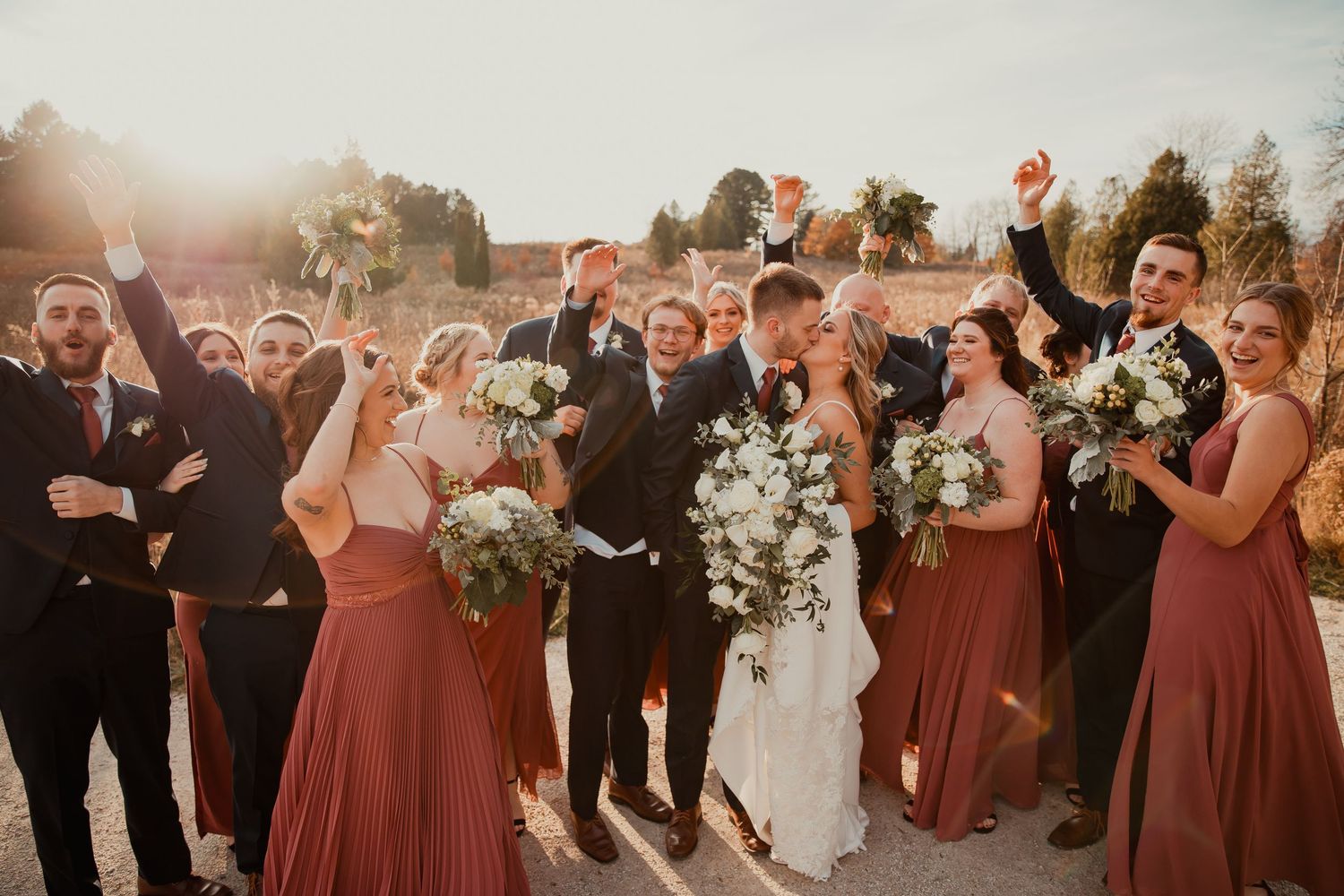 Enthusiastic wedding party cheering together outdoors in burgundy and black formal attire. wedding