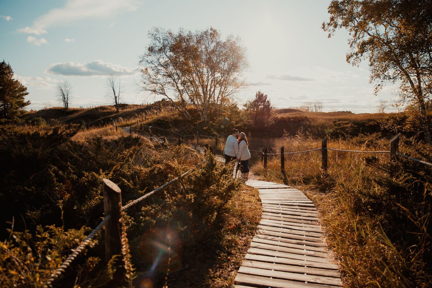 A wooden boardwalk path through golden autumn fields at sunset. couples engagement