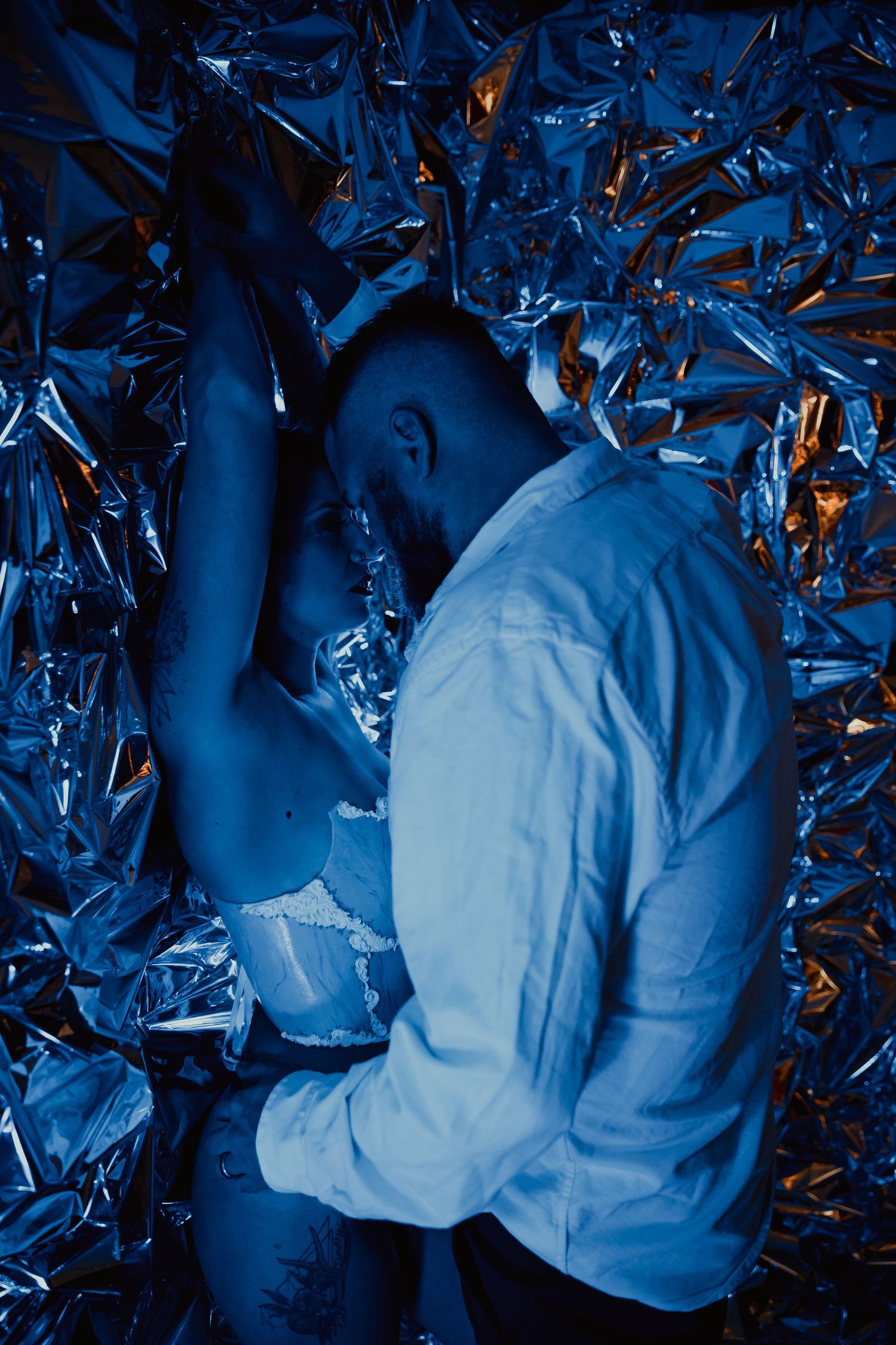 Artistic portrait against metallic blue foil background with dramatic lighting and a white button-up shirt.