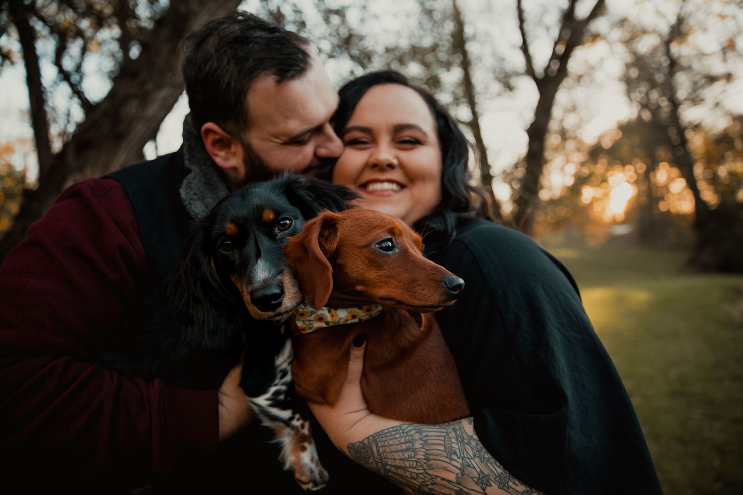 A happy couple shares a tender moment with their playful dachshund dog during sunset in a park. engagement couple