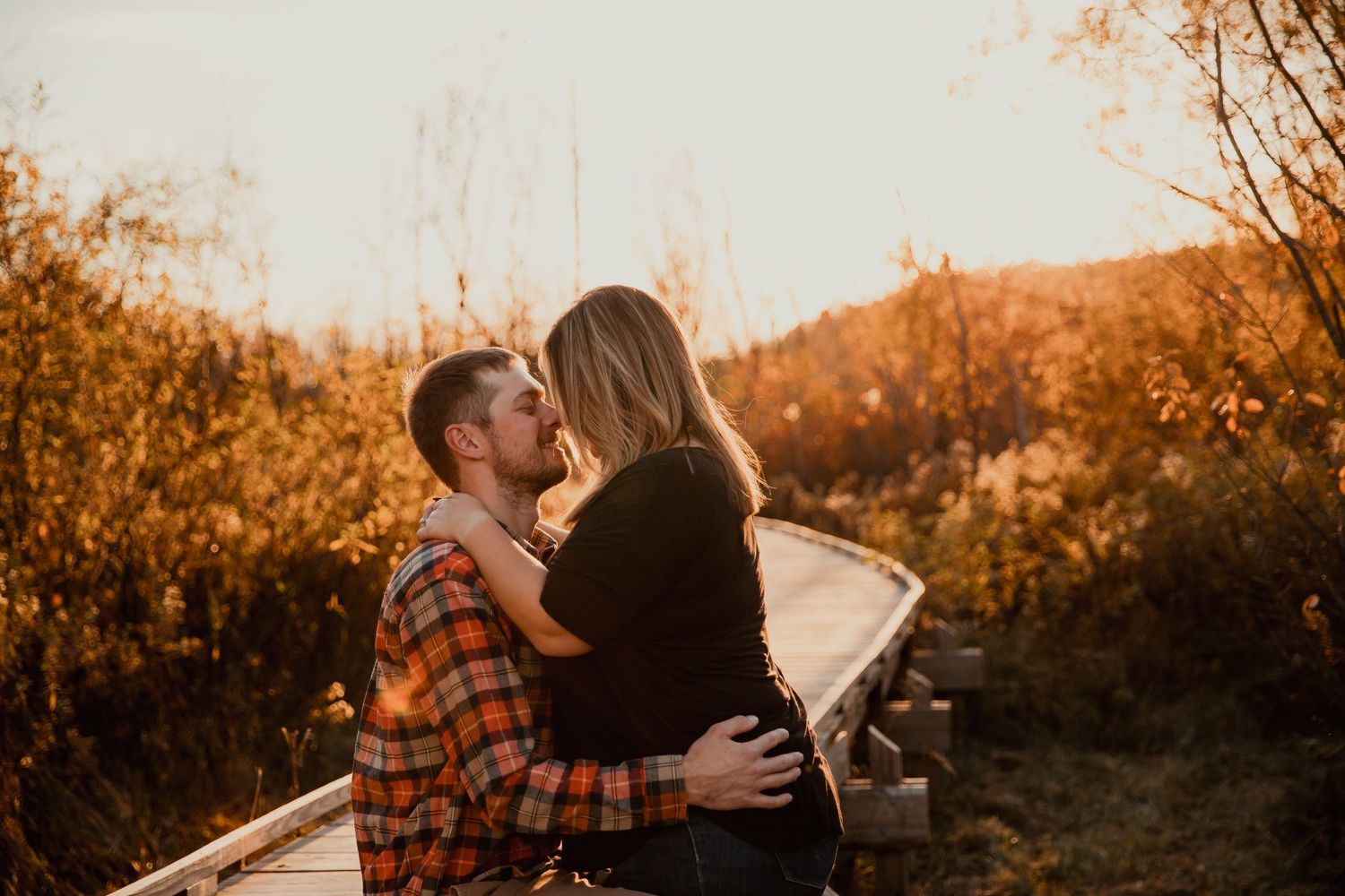A couple shares an intimate moment on a wooden walkway during golden hour. couples engagement