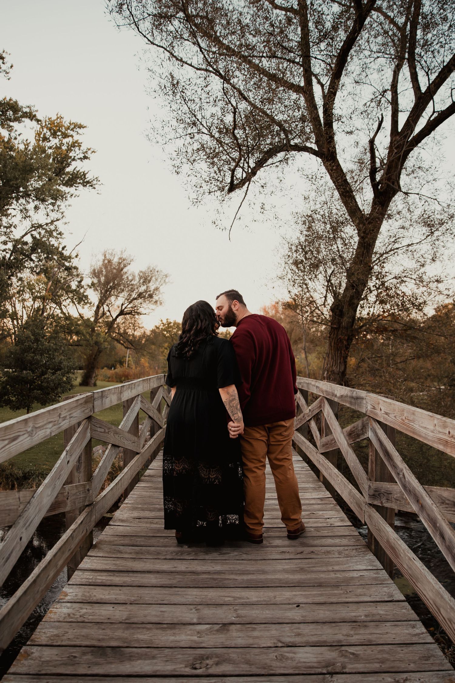 A couple stands close together on a wooden bridge during sunset. couples engagement