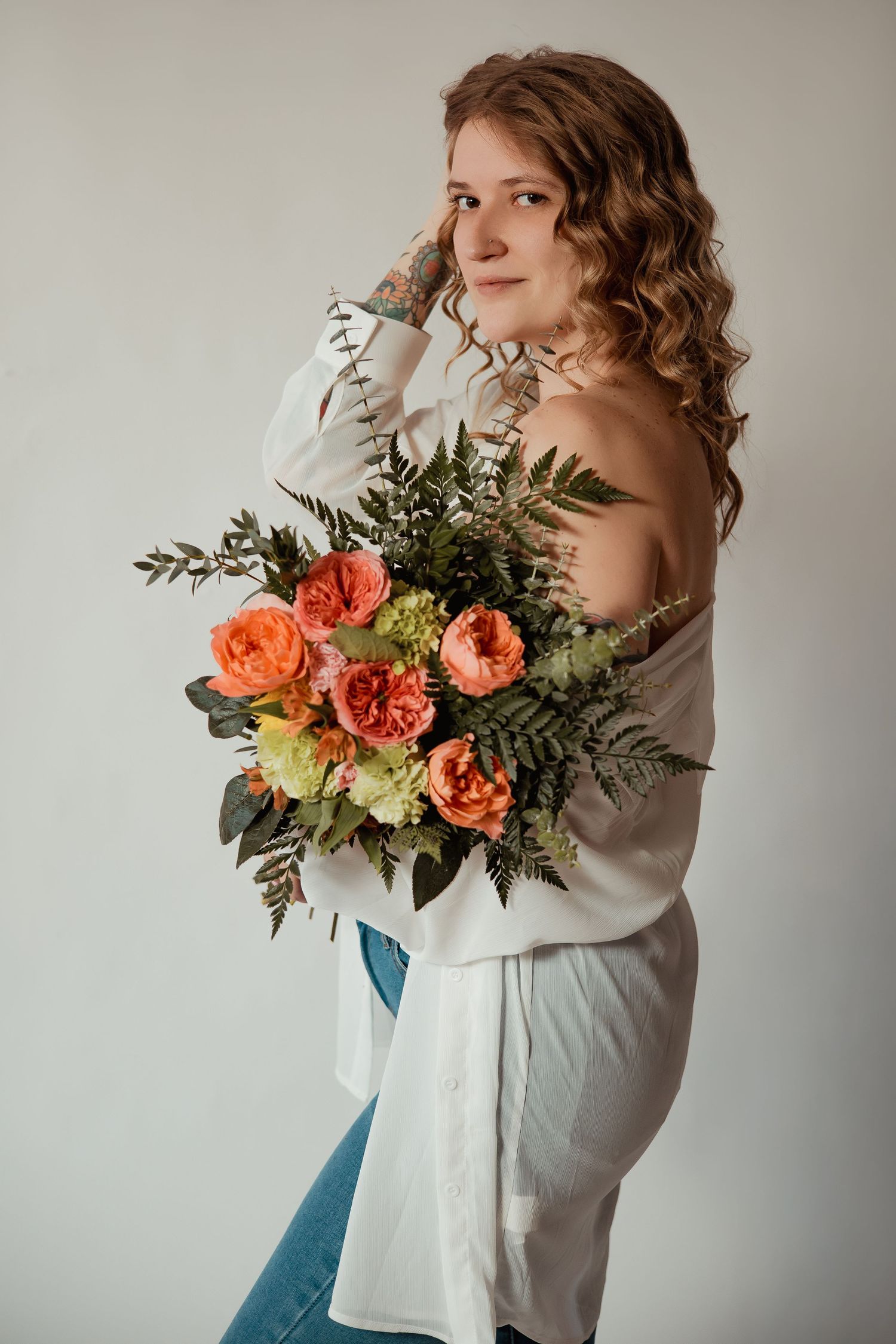 Artistic portrait featuring coral roses and greenery bouquet against neutral background with soft lighting.