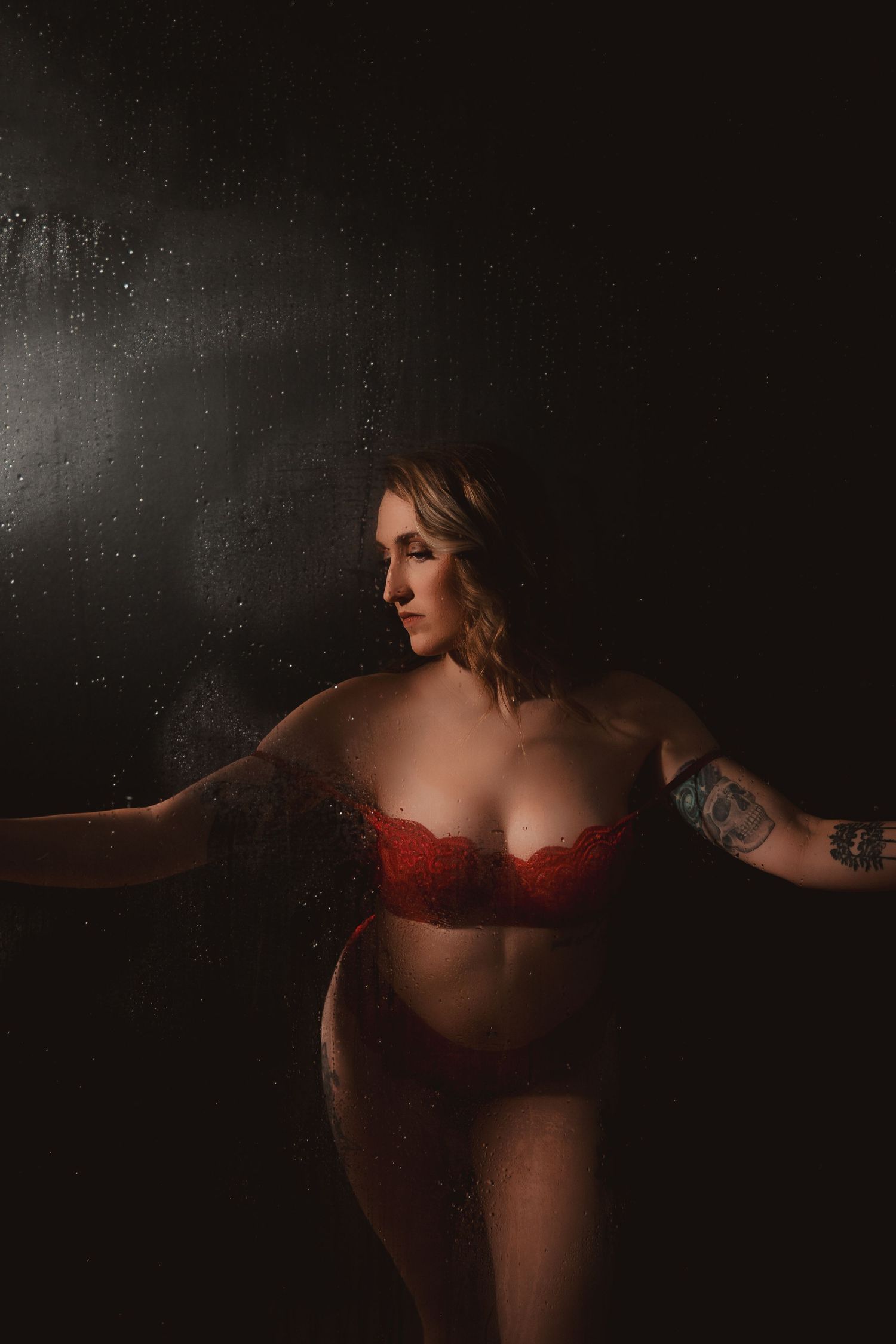 Artistic dark boudoir photograph featuring a figure in red lingerie against a moody black background.