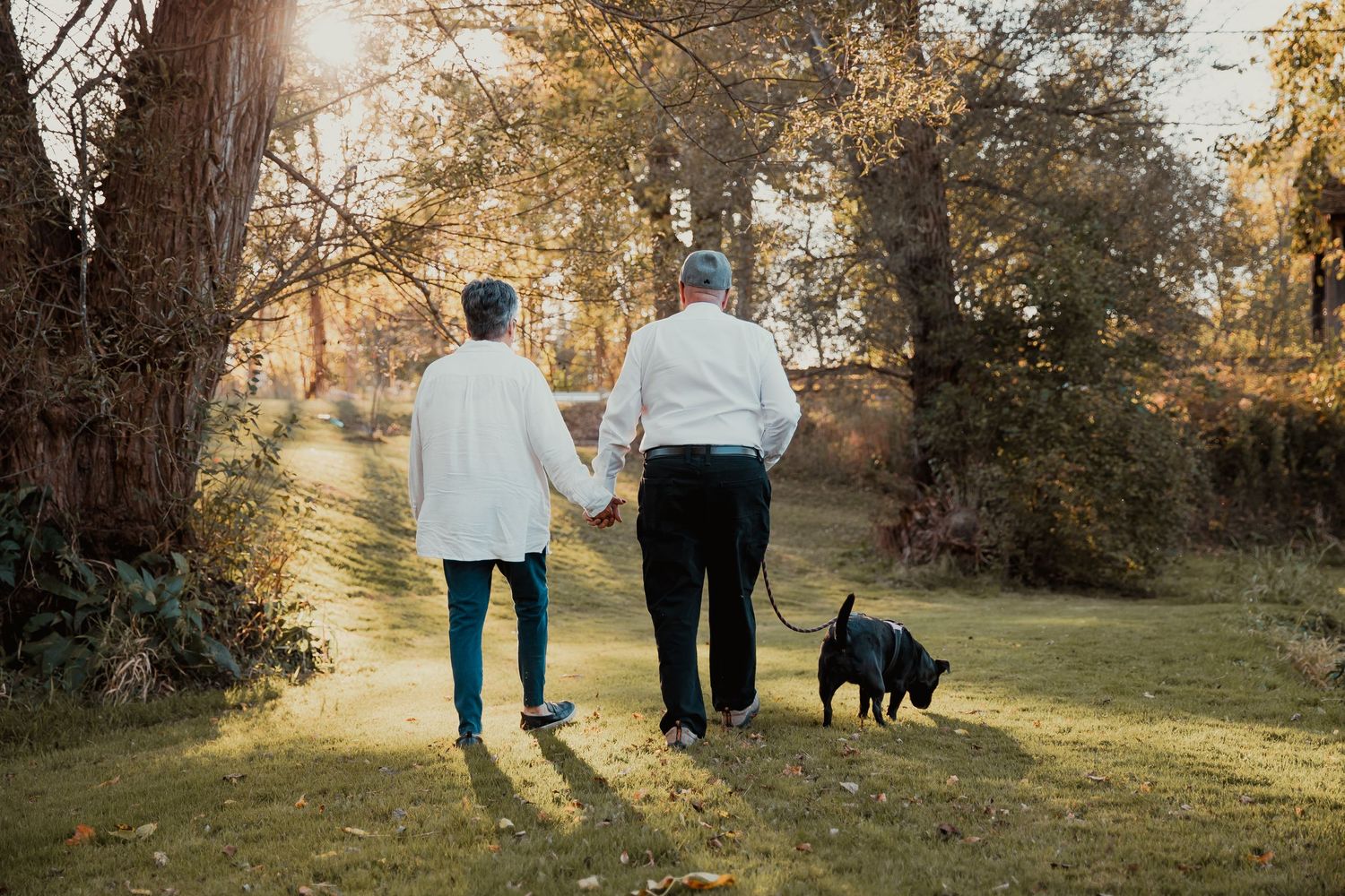 Couple walking with black dog on path through sunlit autumn landscape. couples engagement